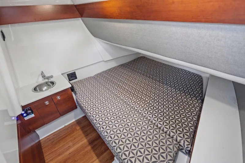 Slide: The Image of 2022 Chaparral 300 OSX cabin interior with bed, sink, and wooden cabinetry. - 21