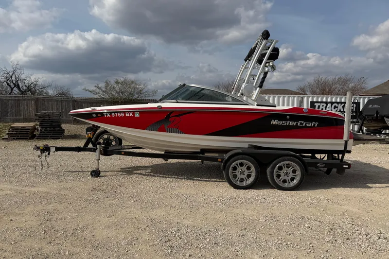 The Image of 2012 MasterCraft X2 boat on trailer, red and white design, parked outdoors. - 1