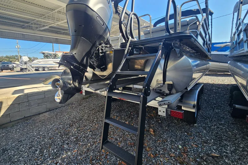 Slide: The Image of 2026 Bentley Pontoons LEGACY 243 QUAD SWINGBACK with outboard motor and ladder, parked on gravel. - 24