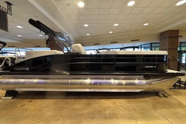 Slide: The Image of 2026 Harris Cruiser 230 pontoon boat displayed indoors, featuring sleek black design. - 1