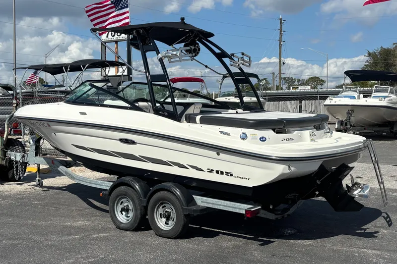 Slide: The Image of 2014 Sea Ray 205 Sport boat on trailer, displayed outdoors with American flags. - 1