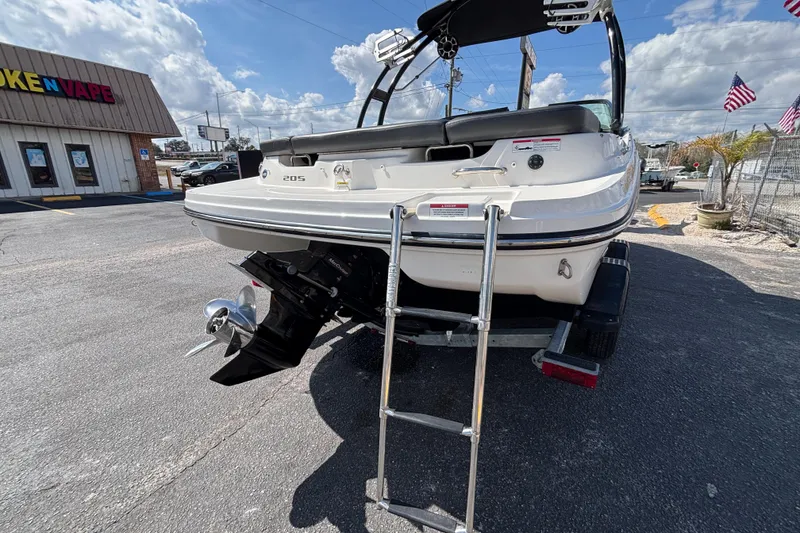 Slide: The Image of 2014 Sea Ray 205 Sport boat with ladder, parked outdoors under a blue sky. - 13