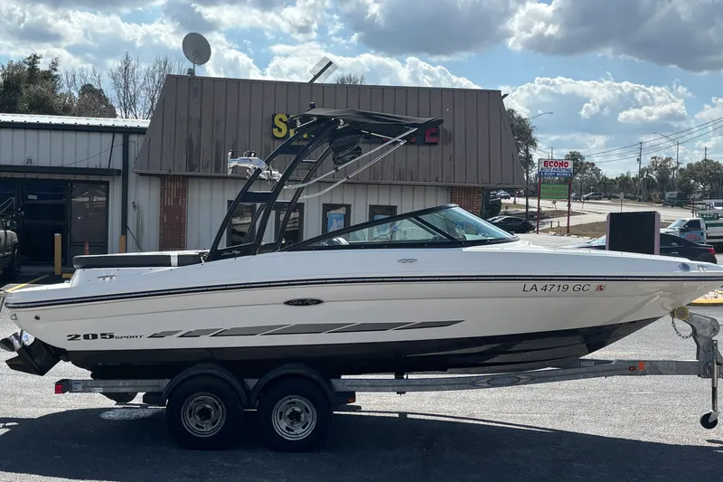 Slide: The Image of 2014 Sea Ray 205 Sport boat on trailer, parked outside a building under a cloudy sky. - 4