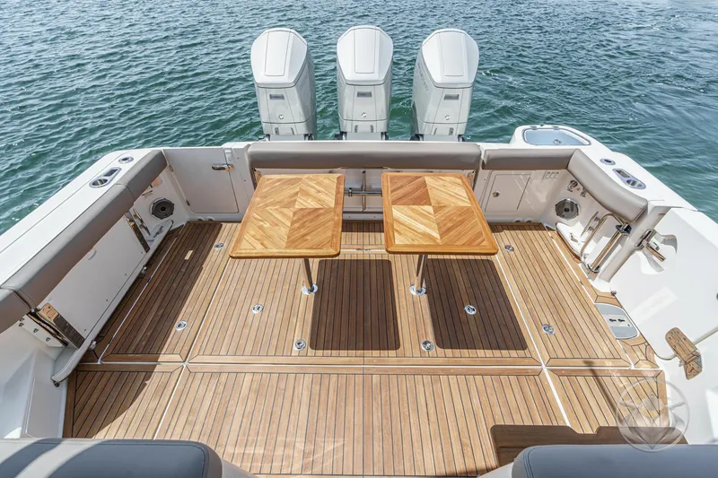 Slide: The Image of 2025 Boston Whaler 405 Conquest boat deck with wooden tables and triple outboard engines. - 3