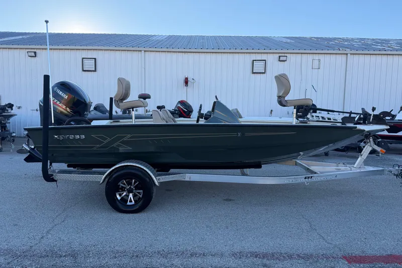 Slide: The Image of 2021 Xpress X18PFC fishing boat on trailer, parked outdoors near a white building. - 33