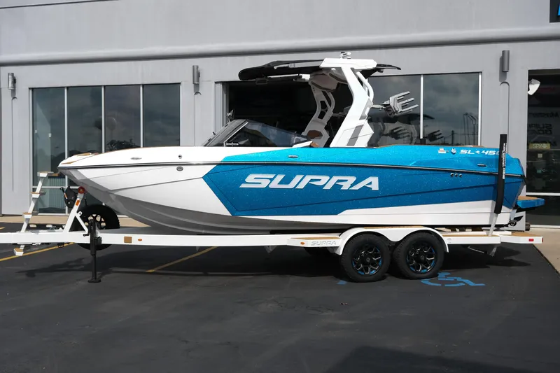 Slide: The Image of 2026 Supra SL boat in blue and white on a trailer outside a building. - 1