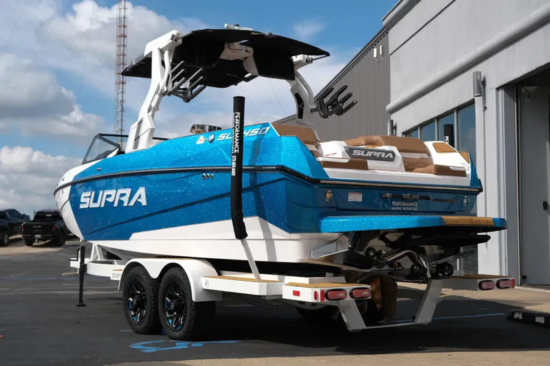 Slide: The Image of 2026 Supra SL boat on trailer, blue and white design, parked outdoors. - 5