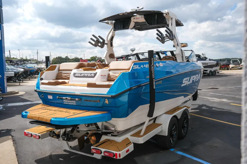 Slide: The Image of 2026 Supra SL boat with blue exterior, parked on a trailer in a marina. - 8