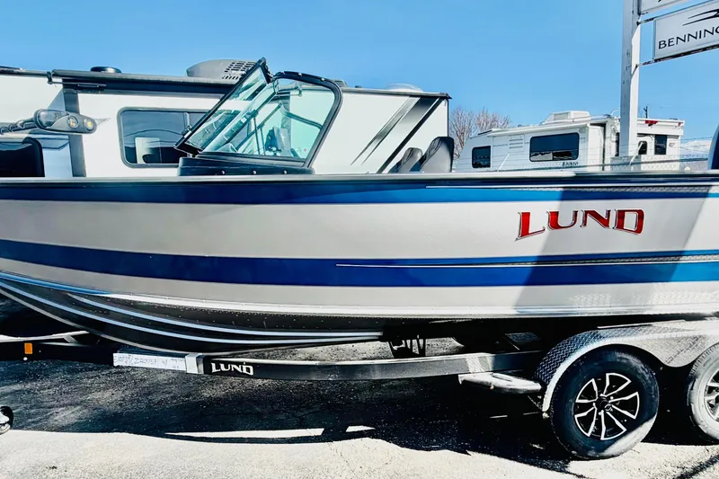 Slide: The Image of 2026 Lund 2075 Fisherman boat on trailer, parked outdoors under clear blue sky. - 2
