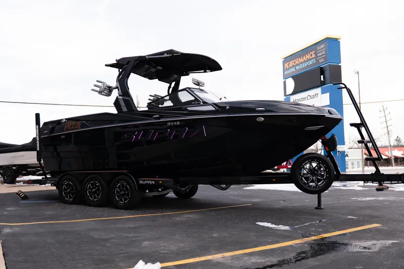 Slide: The Image of 2024 Supra SE boat on trailer at dealership, showcasing sleek black design. - 8