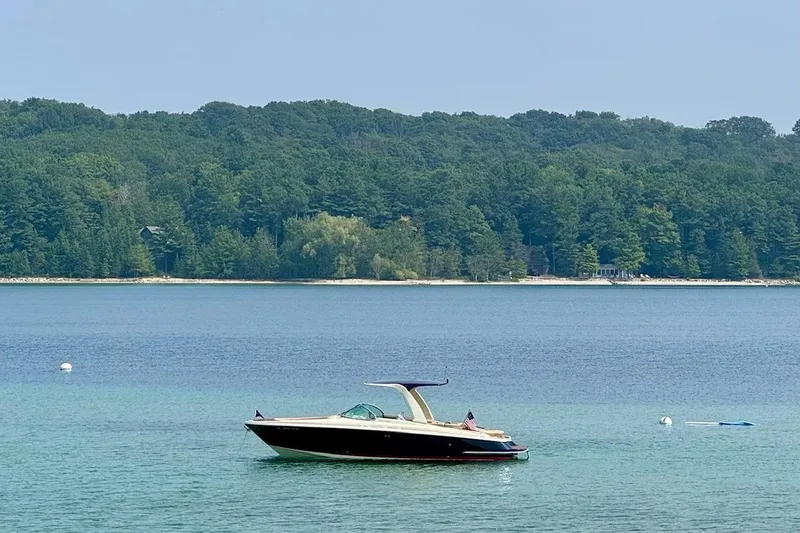 Slide: The Image of 2019 Chris-Craft Launch 28 GT boat on serene lake with forested shoreline. - 7