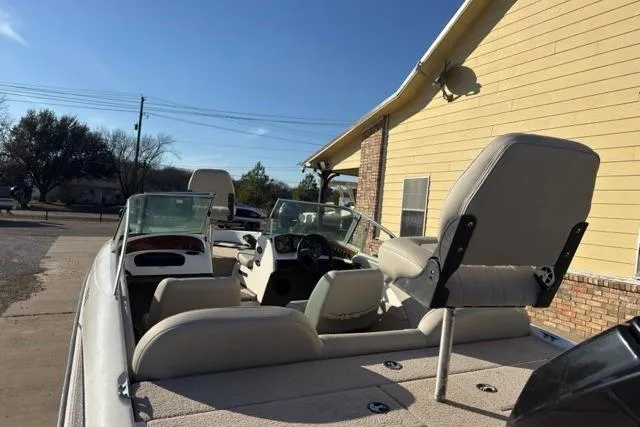 Slide: The Image of 2002 Triton SF-21 boat with beige seating and dual windshields, parked near a yellow building. - 2