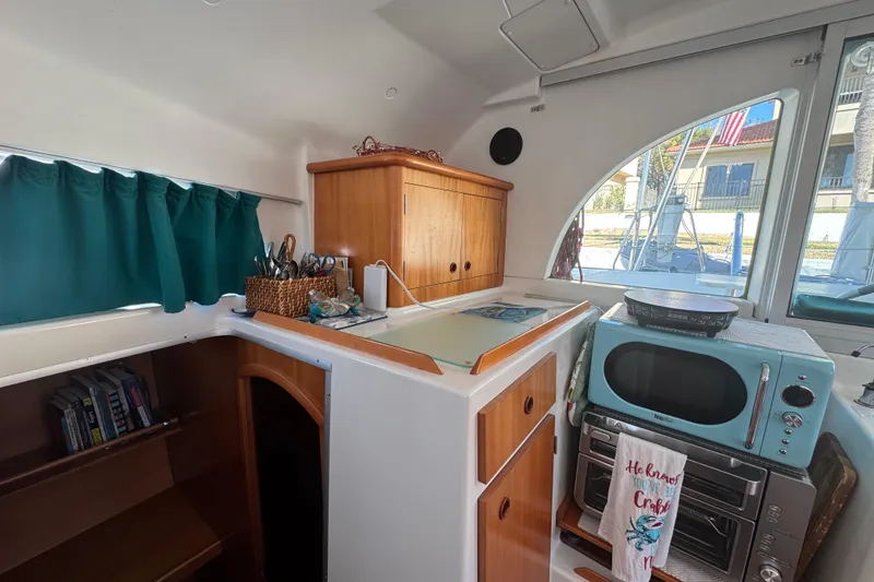 Slide: The Image of Interior of 2000 Lagoon 380 catamaran with kitchenette, teal microwave, and wooden cabinetry. - 13