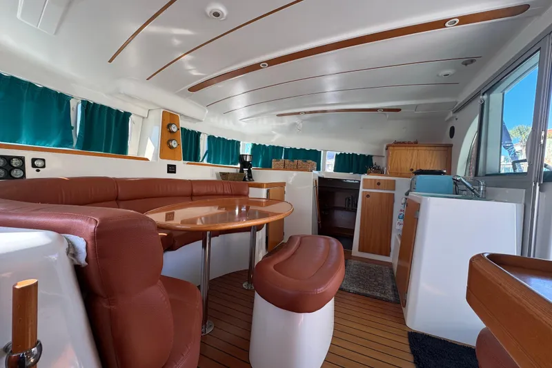Slide: The Image of Interior of 2000 Lagoon 380 catamaran with brown seating, wooden table, and teal curtains. - 7
