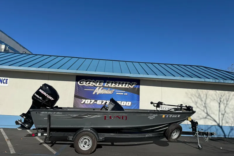 The Image of 2018 Lund 1875 Pro-V Bass boat with Mercury engine on trailer, parked outside a building. - 1