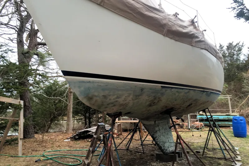 Slide: The Image of 1981 Catalina 30 sailboat on stands, undergoing maintenance in a wooded area. - 12