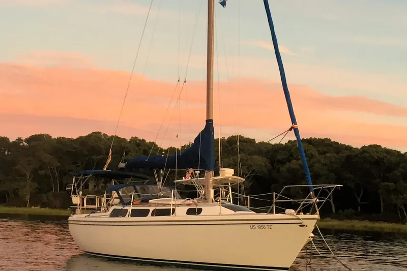 Slide: The Image of 1981 Catalina 30 sailboat anchored at sunset with pink sky and trees in background. - 9