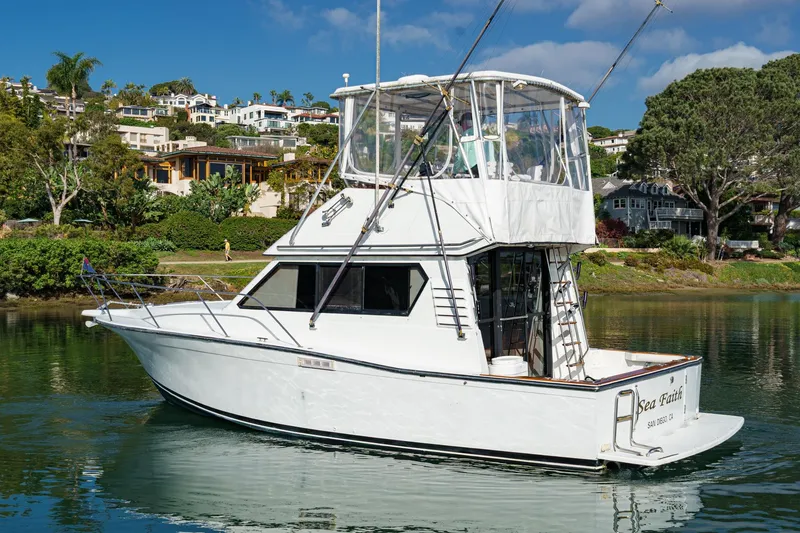 Slide: The Image of 1989 Pearson 34 Convertible yacht on calm water, surrounded by lush greenery and coastal homes. - 2