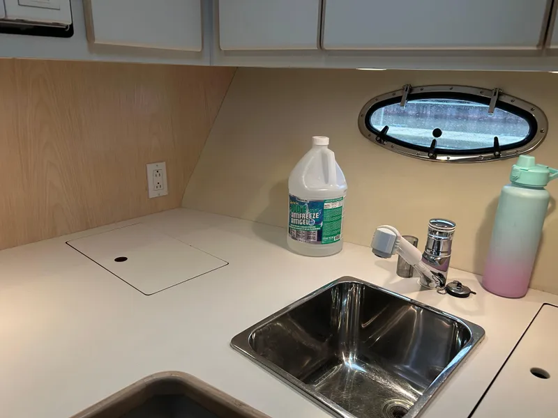 Slide: The Image of 1997 Tiara Yachts 3500 Express kitchen area with sink, cleaning supplies, and porthole window. - 26