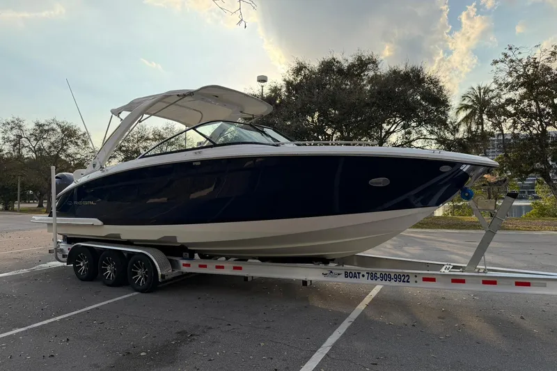 Slide: The Image of 2019 Regal 29 OBX boat on trailer in a parking lot, surrounded by trees. - 2