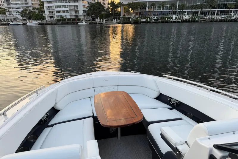 Slide: The Image of 2019 Regal 29 OBX boat interior with elegant seating and wooden table, docked by waterfront buildings. - 36