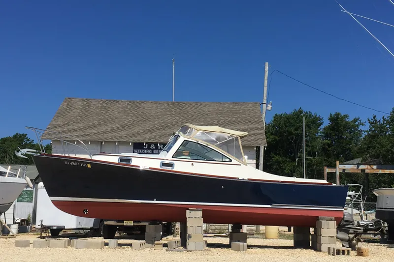 Slide: The Image of 2009 Landing School Arrundel 27 boat on blocks, blue hull, red bottom, outdoor setting. - 6