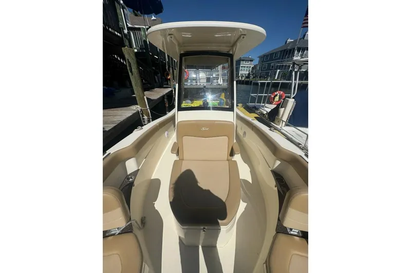 Slide: The Image of 2019 Scout 235 XSF boat interior with tan seating and helm, docked at marina. - 3
