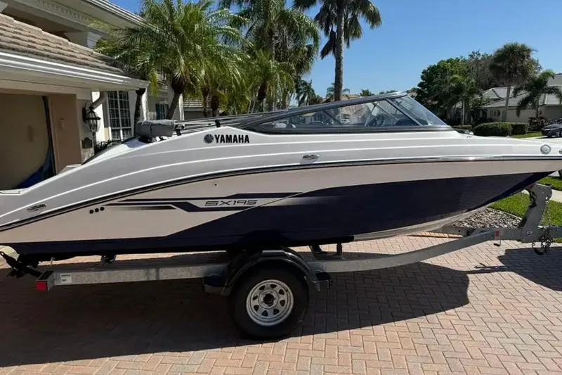 The Image of 2022 Yamaha SX195 boat on trailer, parked in a sunny driveway with palm trees. - 1