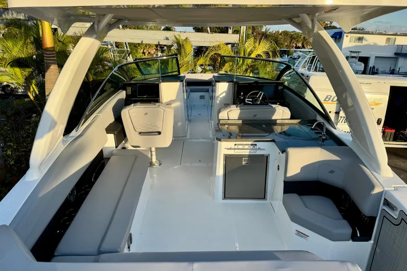 Slide: The Image of 2026 Four Winns H33 OB boat interior with modern seating and helm, surrounded by lush greenery. - 11