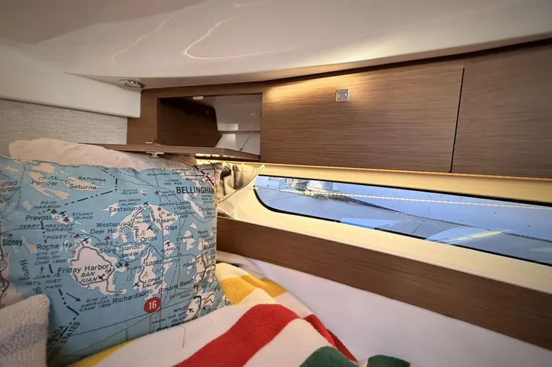 Slide: The Image of Interior of 2022 Jeanneau NC Weekender 895 with map-themed pillow and wooden cabinetry. - 35