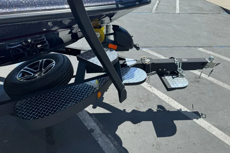 Slide: The Image of 2026 Triton 18 TrX boat trailer with diamond plate steps and spare tire in parking lot. - 3
