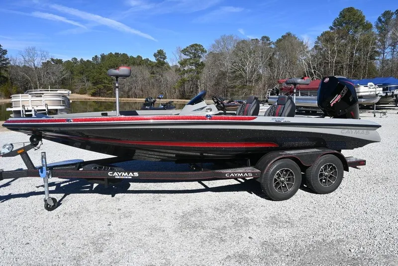 The Image of 2025 Caymas 201 Pro boat on trailer, parked near a lake with trees in background. - 1