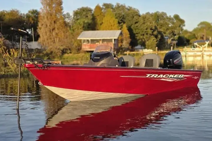 The Image of Red 2021 Tracker Super Guide V-16 SC boat on calm water, surrounded by trees and a dock. - 2