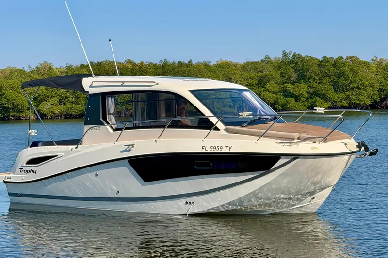 The Image of 2024 Bayliner Trophy T25 Explorer boat on calm water, surrounded by lush greenery. - 0