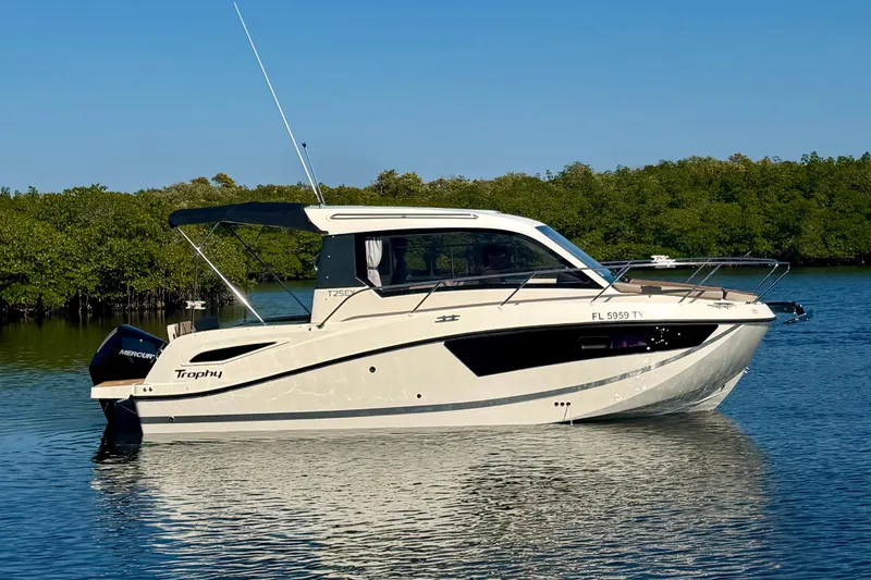 Slide: The Image of 2024 Bayliner Trophy T25 Explorer boat on calm water, surrounded by lush greenery. - 1