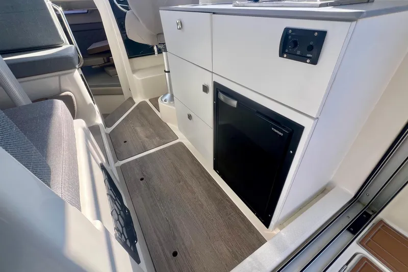 Slide: The Image of 2024 Bayliner Trophy T25 Explorer interior with modern cabinetry and compact refrigerator. - 12