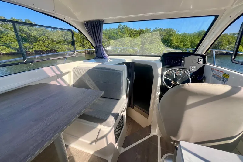 Slide: The Image of 2024 Bayliner Trophy T25 Explorer interior with helm, seating, and table, surrounded by water views. - 7