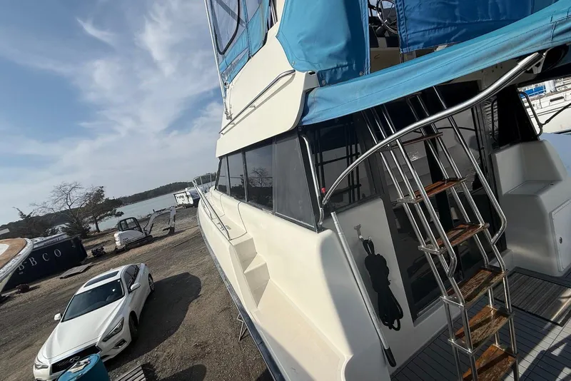 Slide: The Image of 1990 Silverton 37 Convertible yacht with blue canopy, docked near a white car and scenic lake. - 9