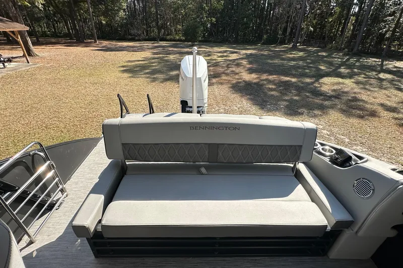 Slide: The Image of 2023 Bennington LX 26 Swingback boat with cushioned seating, parked on grassy area. - 11