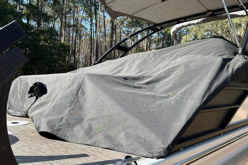 Slide: The Image of 2023 Bennington LX 26 Swingback boat covered, surrounded by trees. - 18