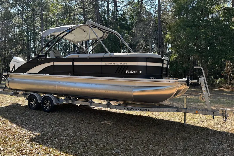 Slide: The Image of 2023 Bennington LX 26 Swingback pontoon boat on trailer in wooded area. - 3