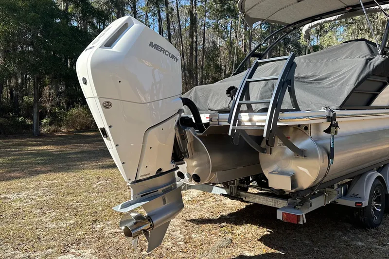 Slide: The Image of 2023 Bennington LX 26 Swingback pontoon boat with Mercury outboard engine in wooded area. - 6