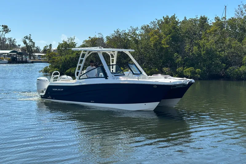 The Image of 2026 World Cat 265 DC-X boat cruising on a calm river with lush greenery. - 0