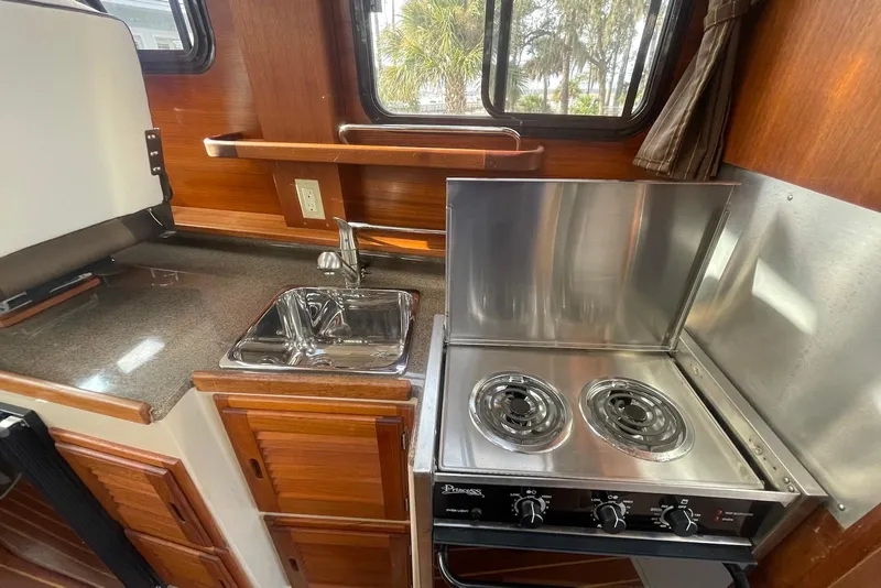 Slide: The Image of 2012 Ranger Tugs R-27 boat kitchen with stove, sink, and wooden cabinetry. - 11