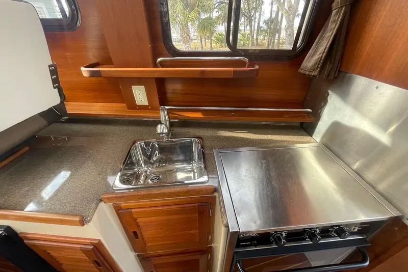 Slide: The Image of 2012 Ranger Tugs R-27 boat kitchen with sink, stove, and wooden cabinetry. - 12