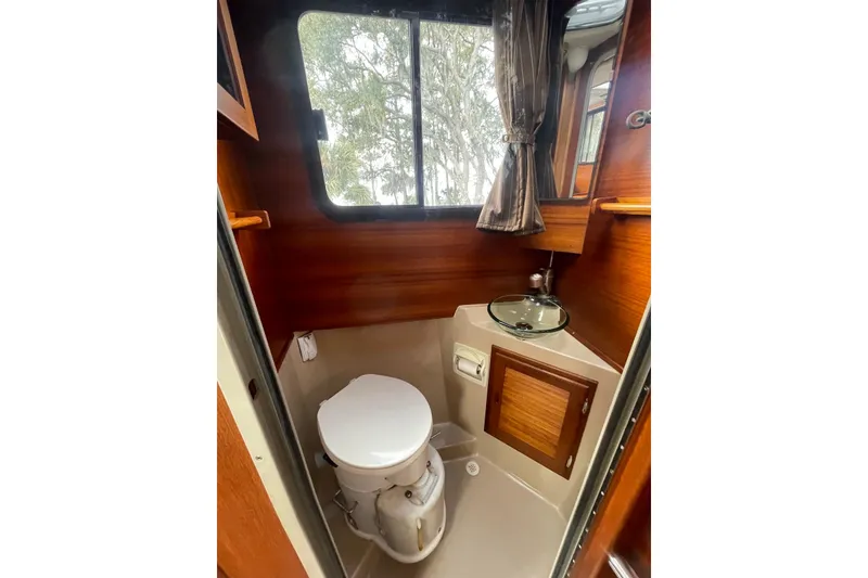 Slide: The Image of 2012 Ranger Tugs R-27 boat bathroom with toilet, sink, and wooden cabinetry. - 19