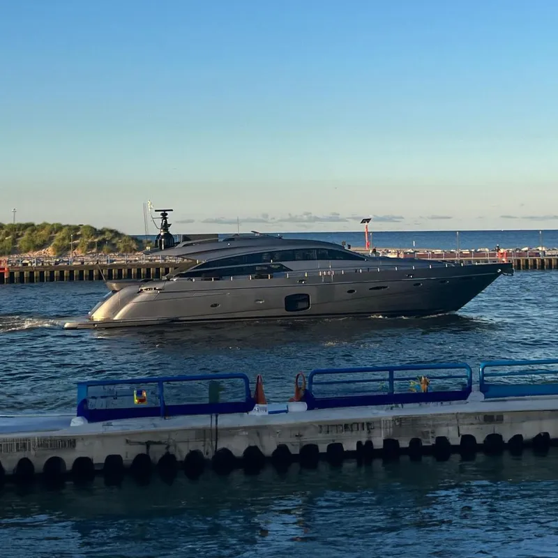 The Image of 2017 Pershing 92 Motor Yacht cruising near a coastal pier under a clear blue sky. - 0