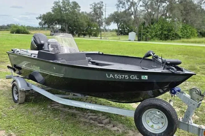 Slide: The Image of 2021 Lowe Fishing Machine 1775SC on trailer, parked on grassy area with trees in background. - 27