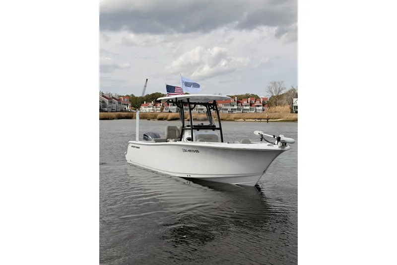The Image of 2022 Sportsman Open 242 Center Console boat on calm water, with flags and residential backdrop. - 0