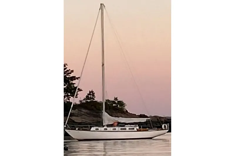 Slide: The Image of Vintage 1969 Tartan 37 sailboat at sunset, anchored near rocky shoreline. - 0